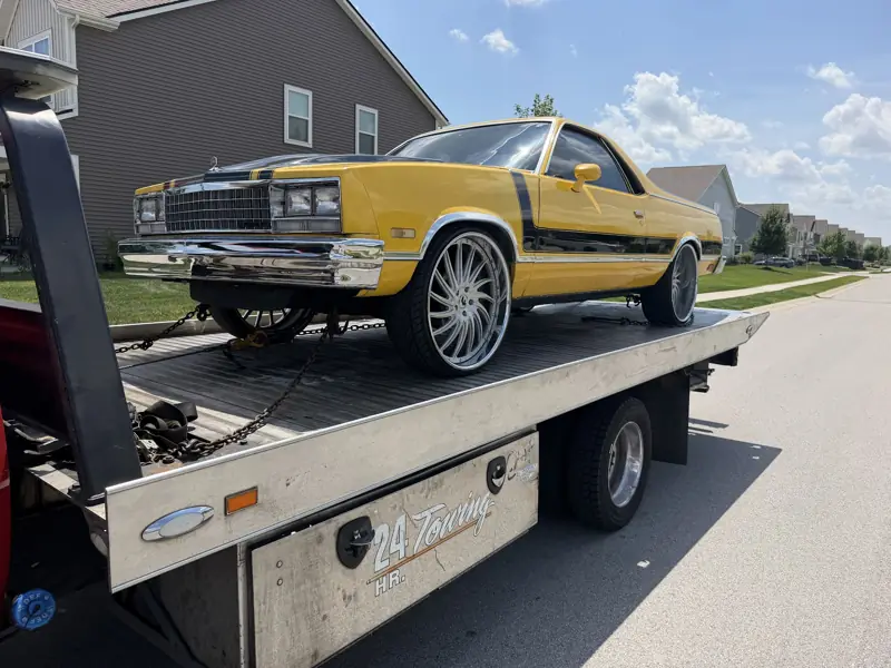 Classic yellow car strapped down on an Elite Detroit Towing flatbed